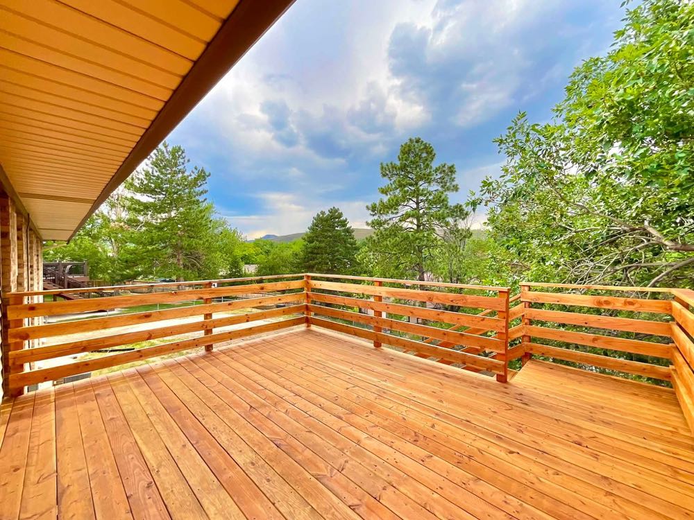 New wooden deck with horizontal wood railing and pine trees