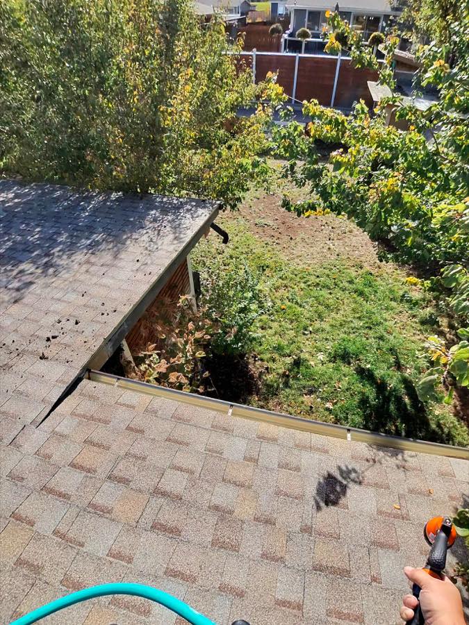 Shingle roof edge where an upper roof meets a lower roof and gutter