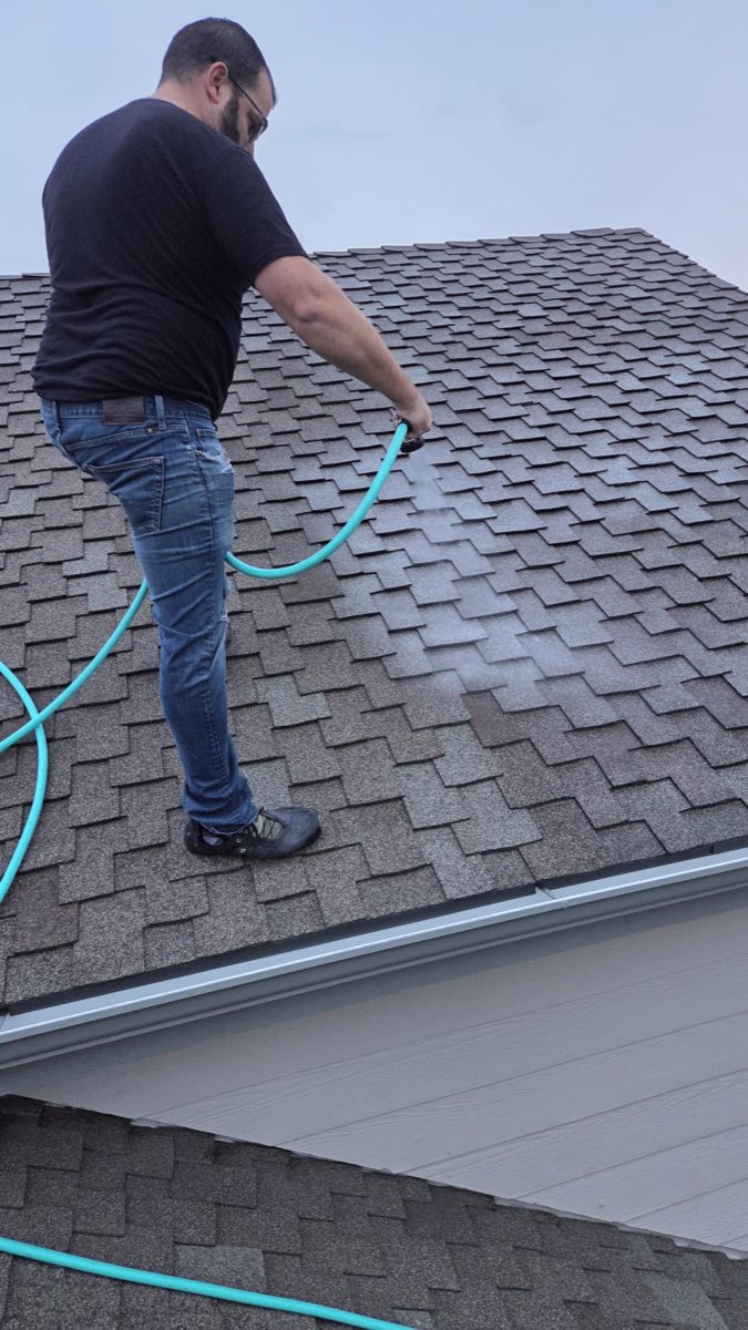 Roofer spraying a rejuvenation treatment onto asphalt shingles